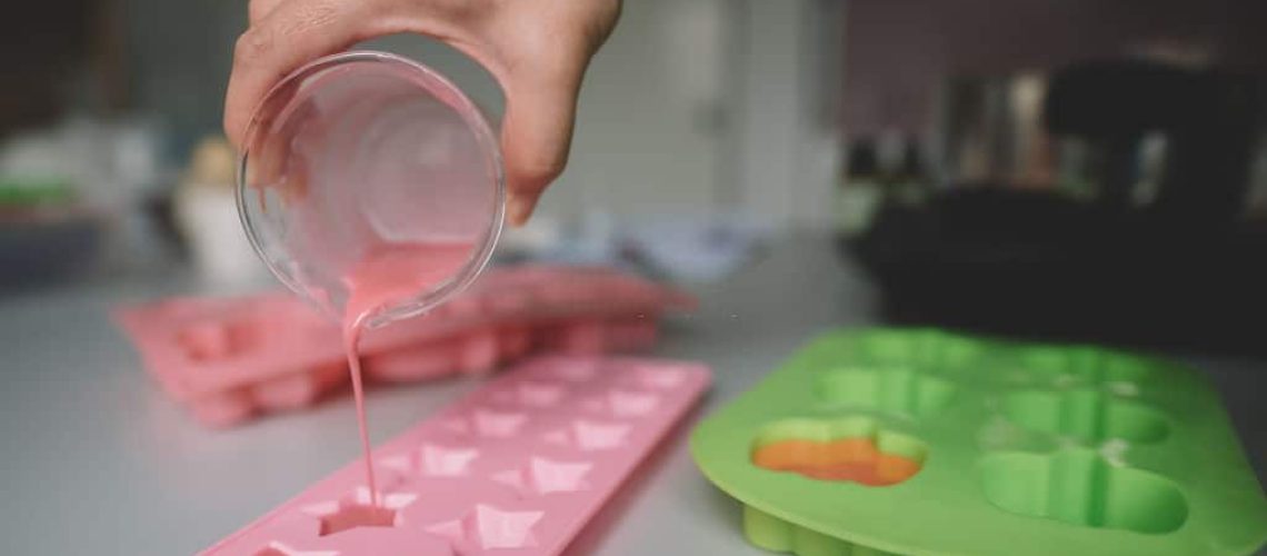 human hand holding the glass and pouring the ingredient into the molding container for homemade soap making